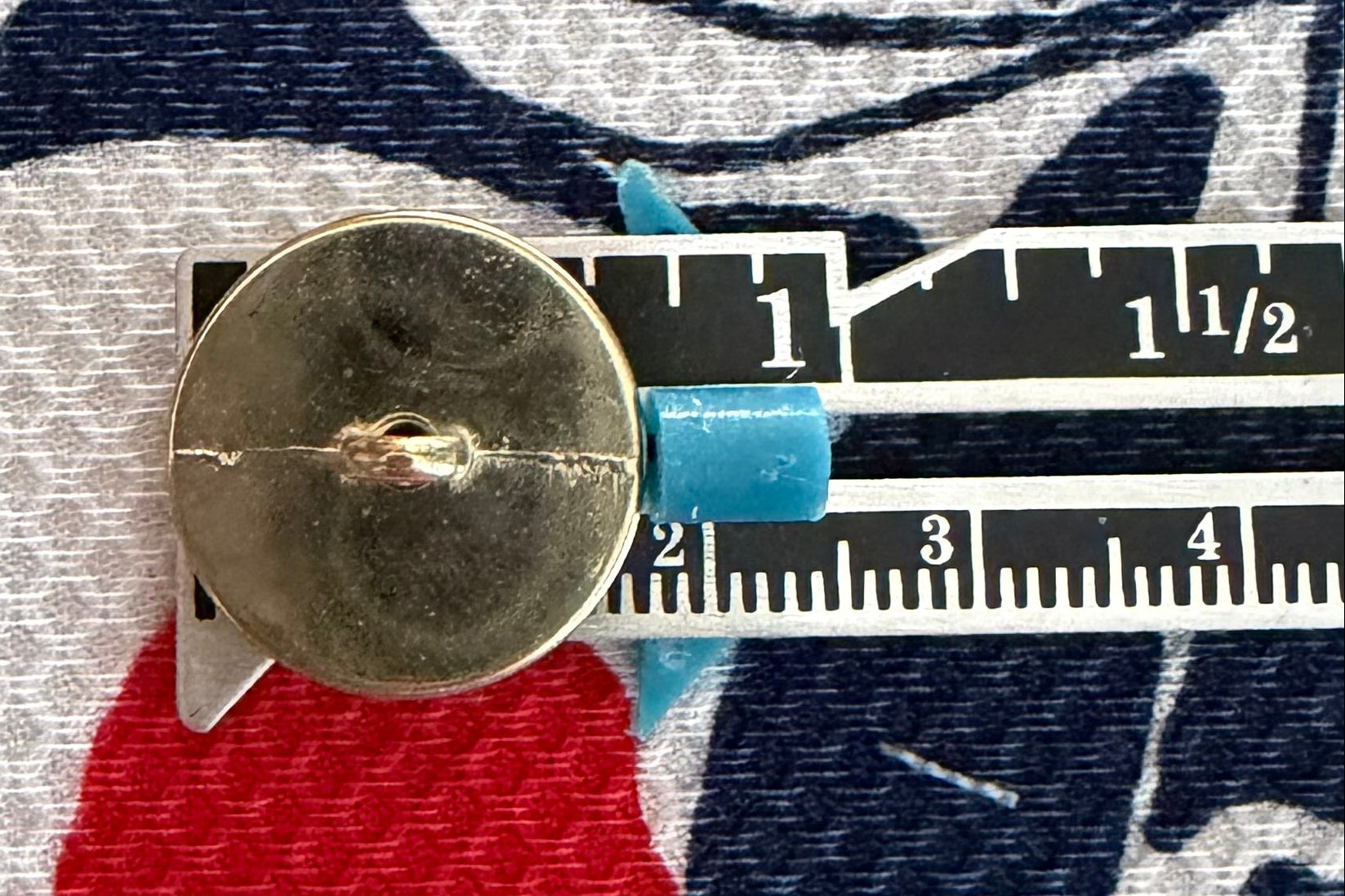 Ruler measuring button width, placed on fabric with floral pattern.