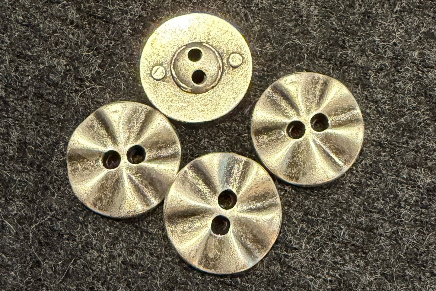 Four metal buttons on a textured dark fabric background