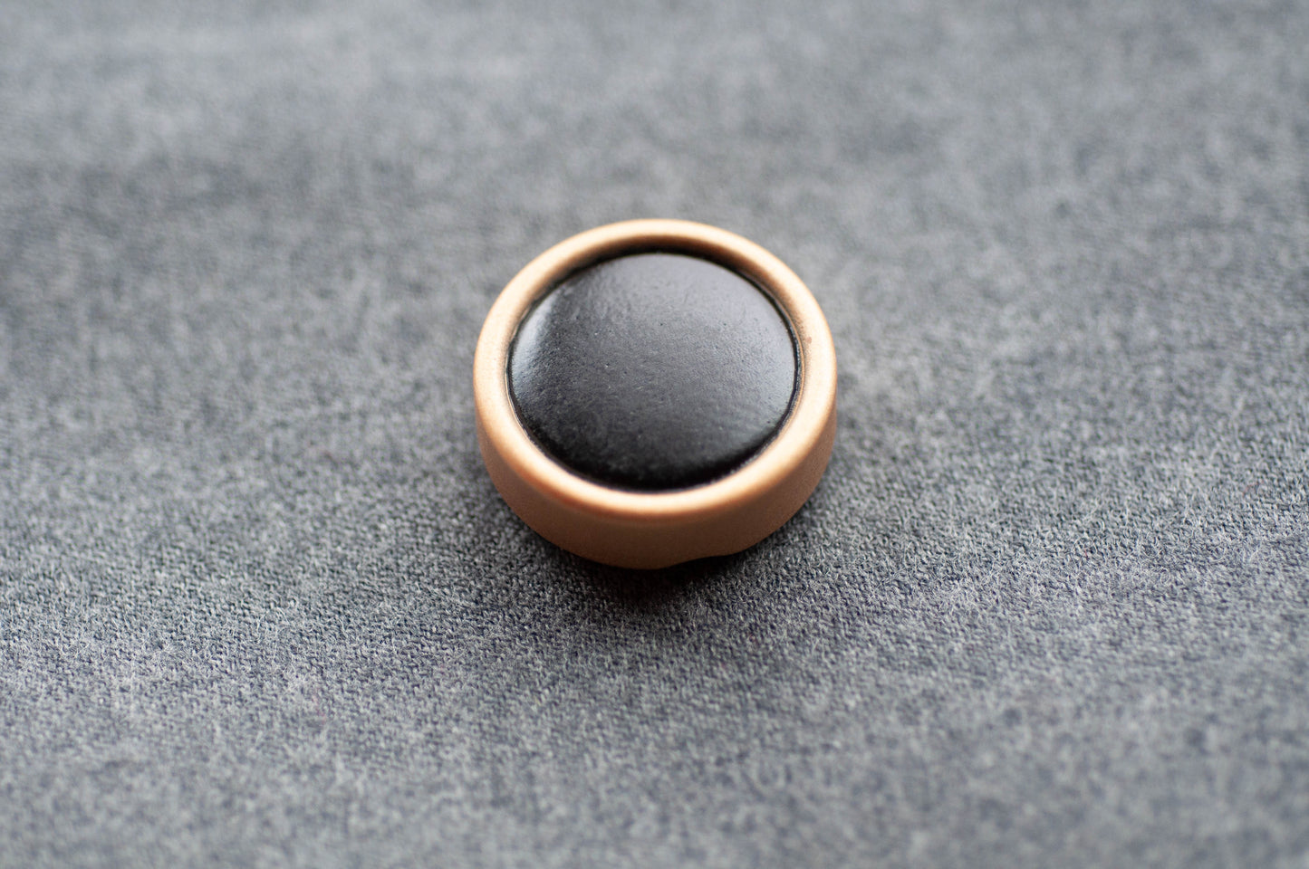 Round black object with bronze border on a gray textured surface