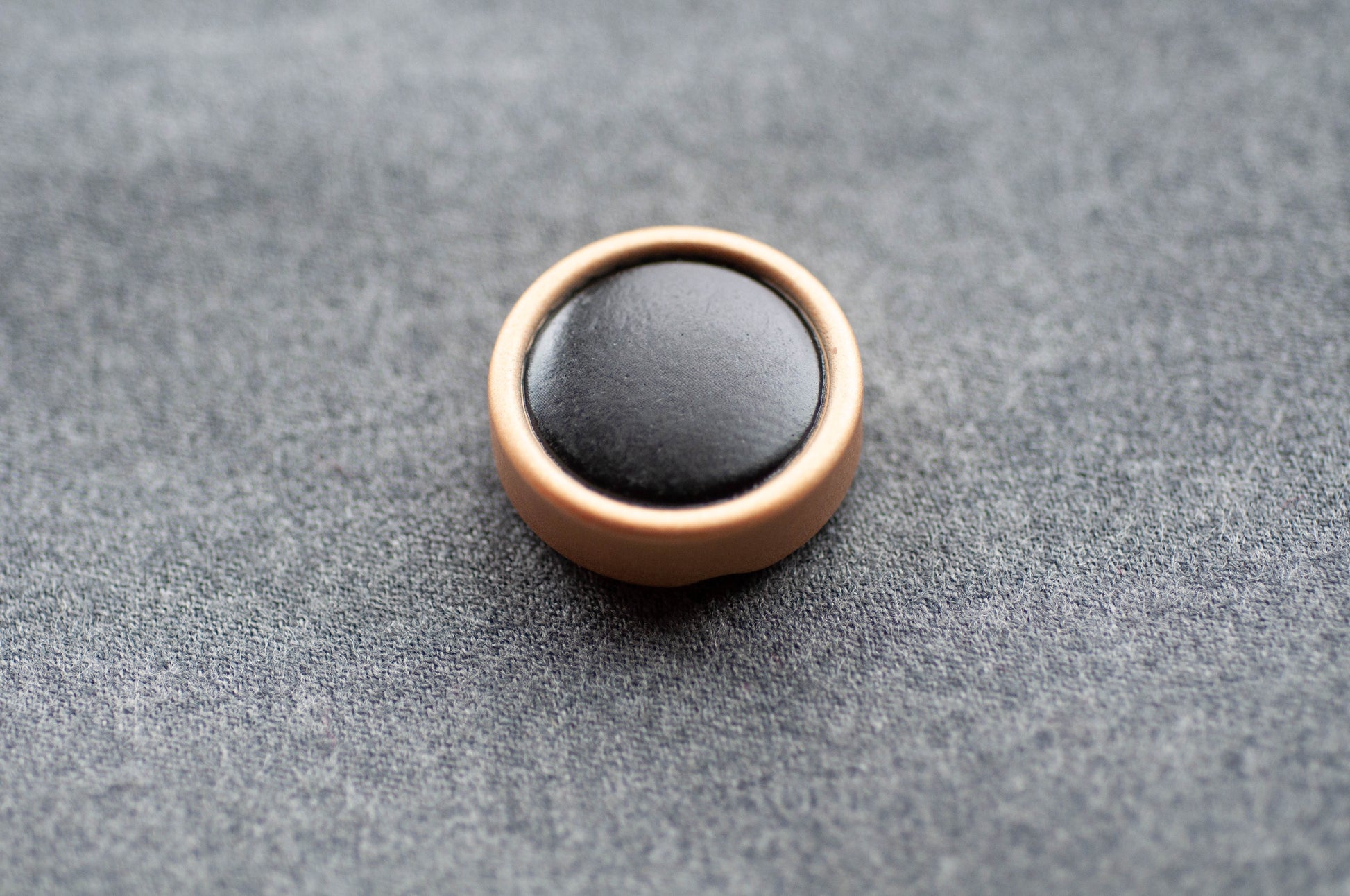 Round black object with bronze border on a gray textured surface