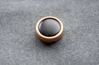 Round black object with bronze border on a gray textured surface