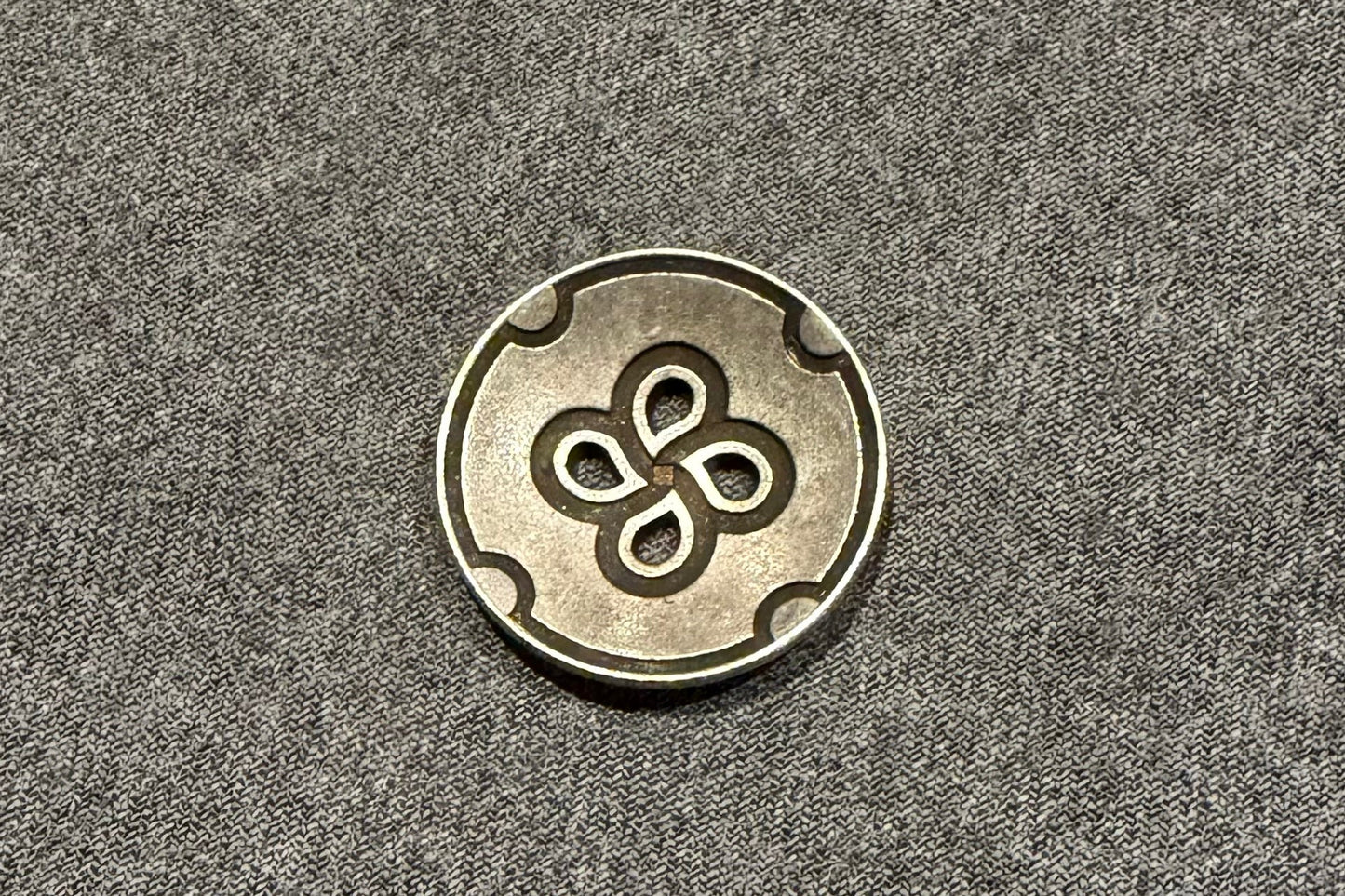Metallic button with a four-leaf clover design on a gray fabric background