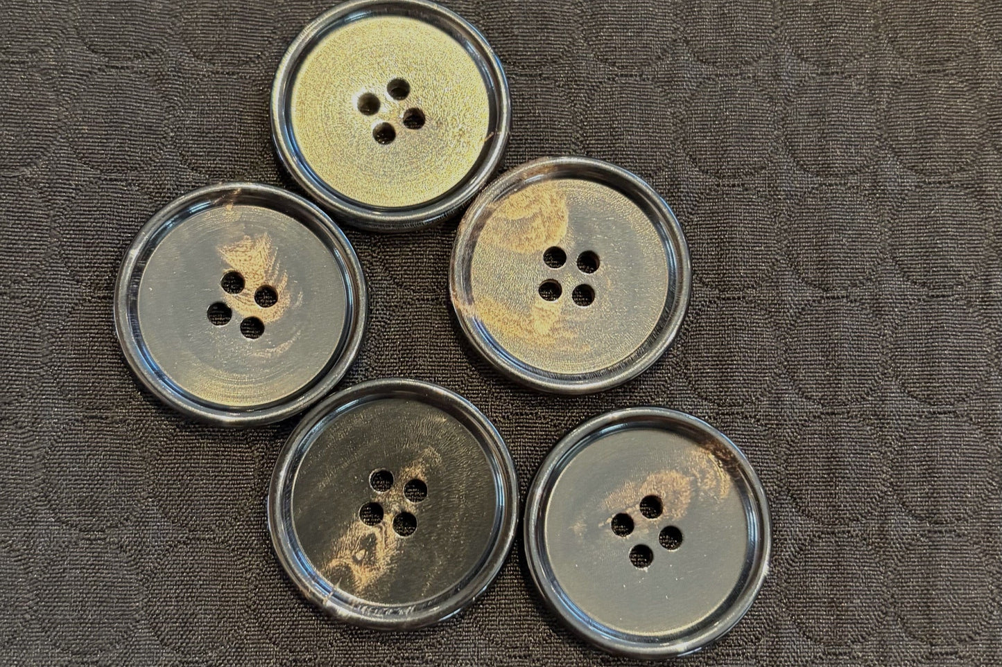 Five black and gold buttons with four holes on a textured black surface