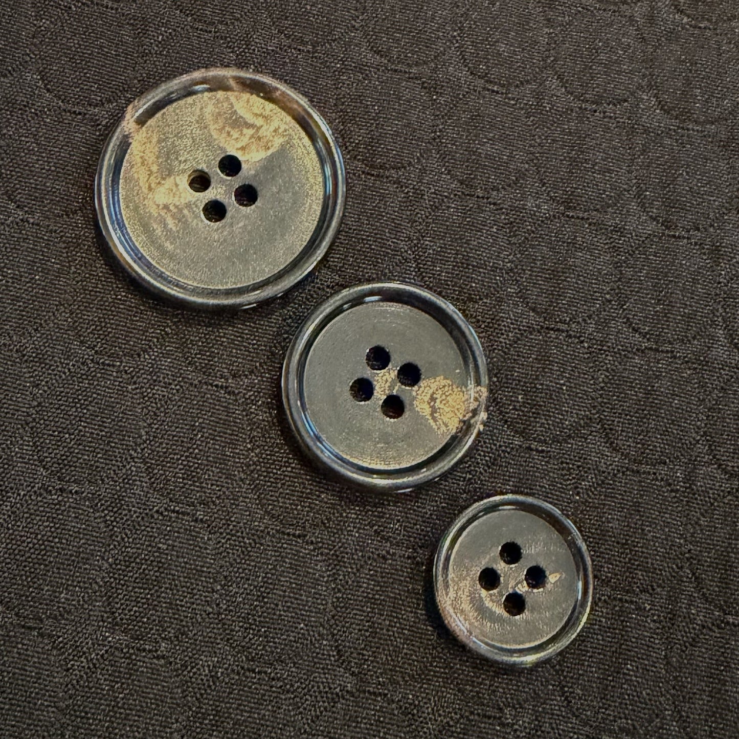 Three horn buttons on a textured dark fabric background
