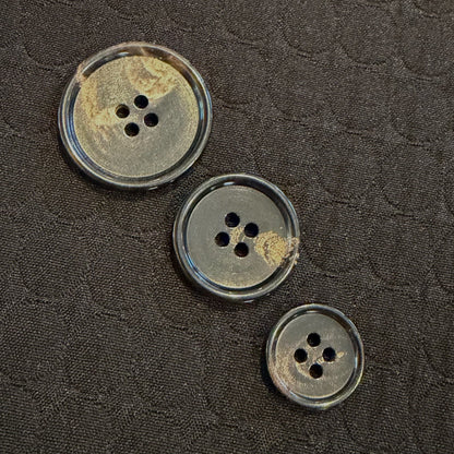 Three horn buttons on a textured dark fabric background