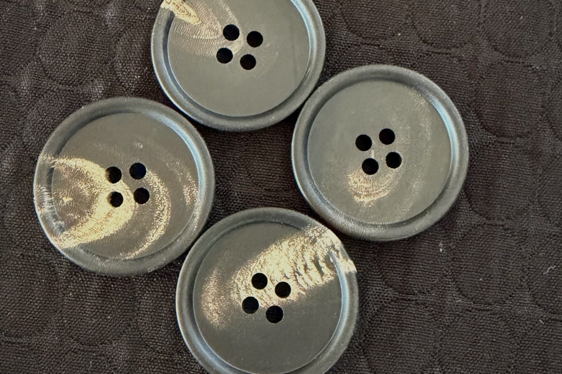 Four black buttons with four holes on a textured dark surface