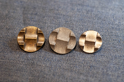 Three metallic buttons with a geometric pattern on a textured fabric background